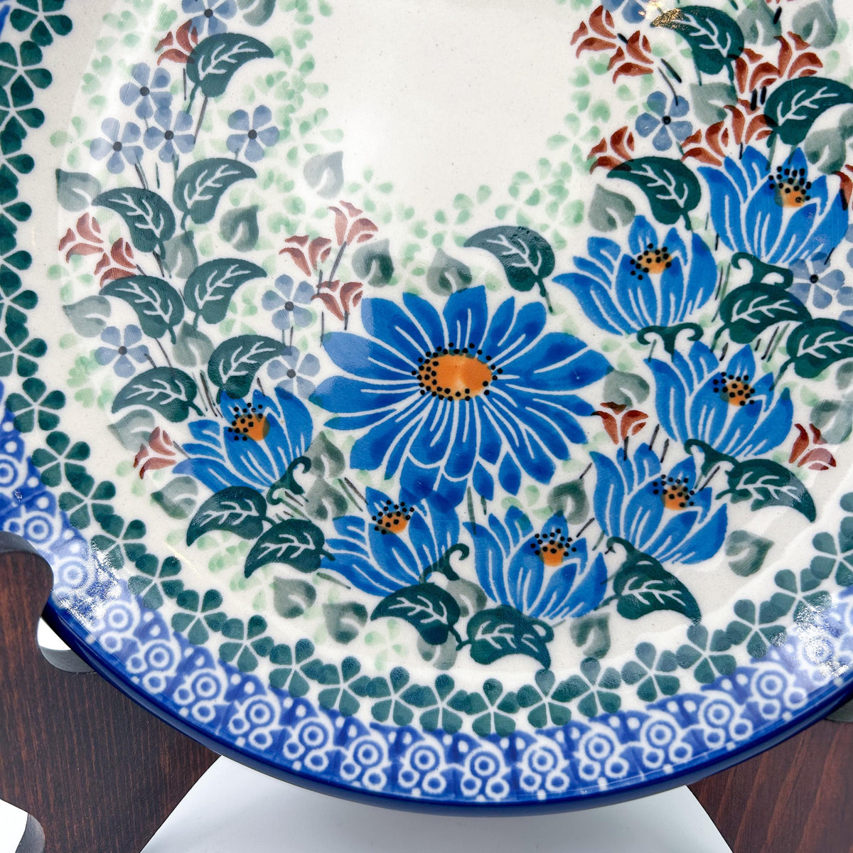 UNIKAT Blue Beauty plate, close-up view of blue daisy bouquet and scalloped border on stand