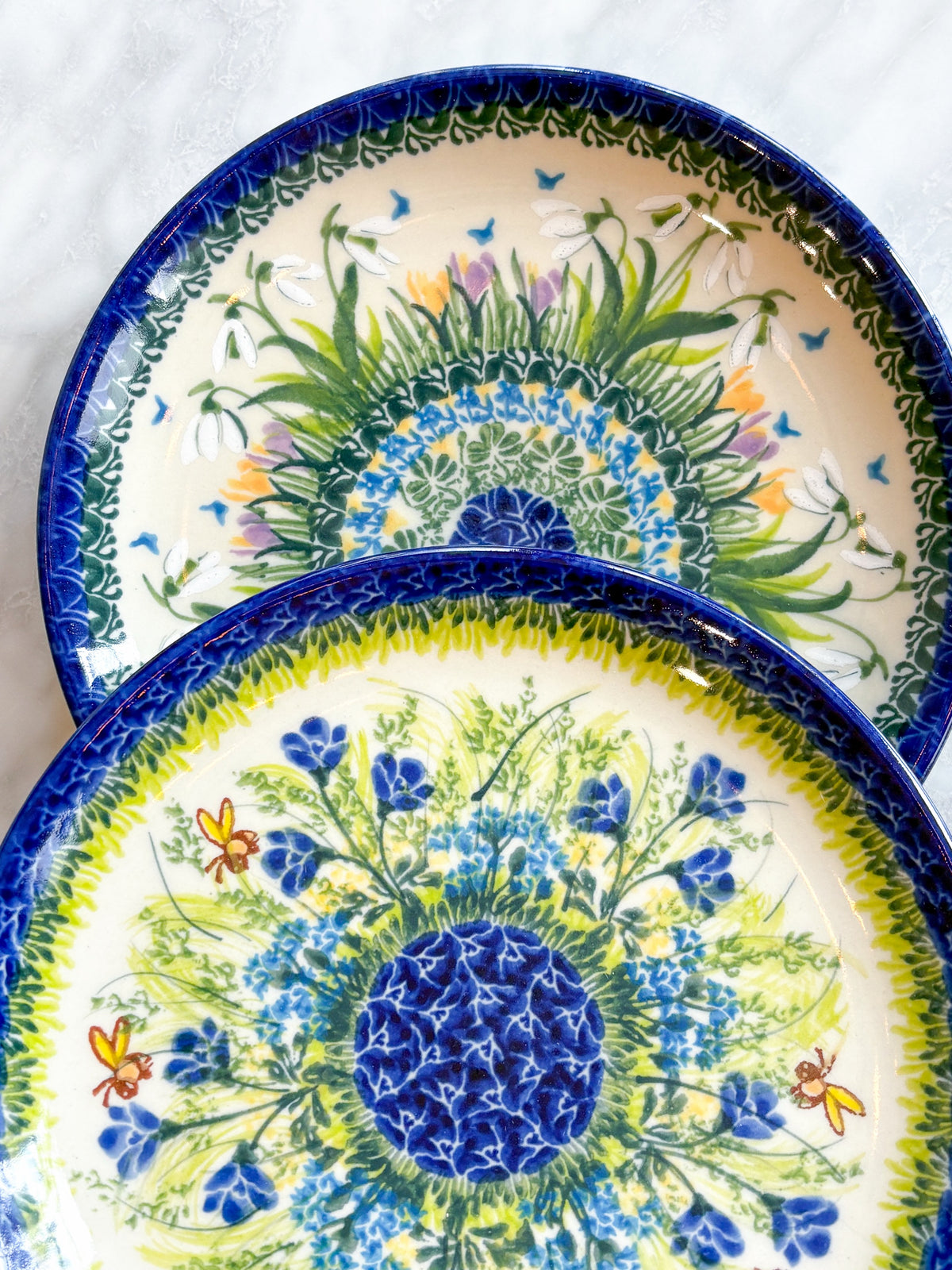 Close view of two hand-painted Polish pottery plates, showing individual brushstrokes in the snowdrop and cornflower patterns