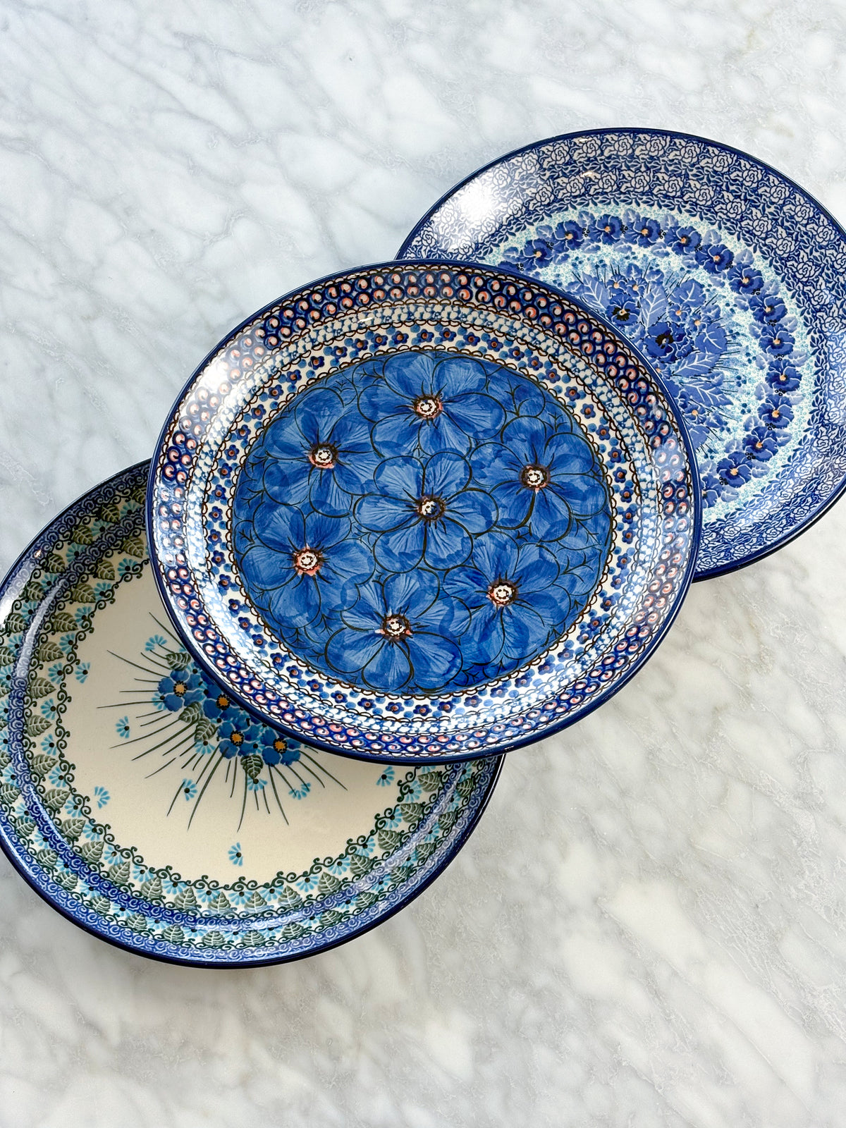 Three hand-painted Polish pottery plates fanned out on a marble counter, each in a different UNIKAT pattern